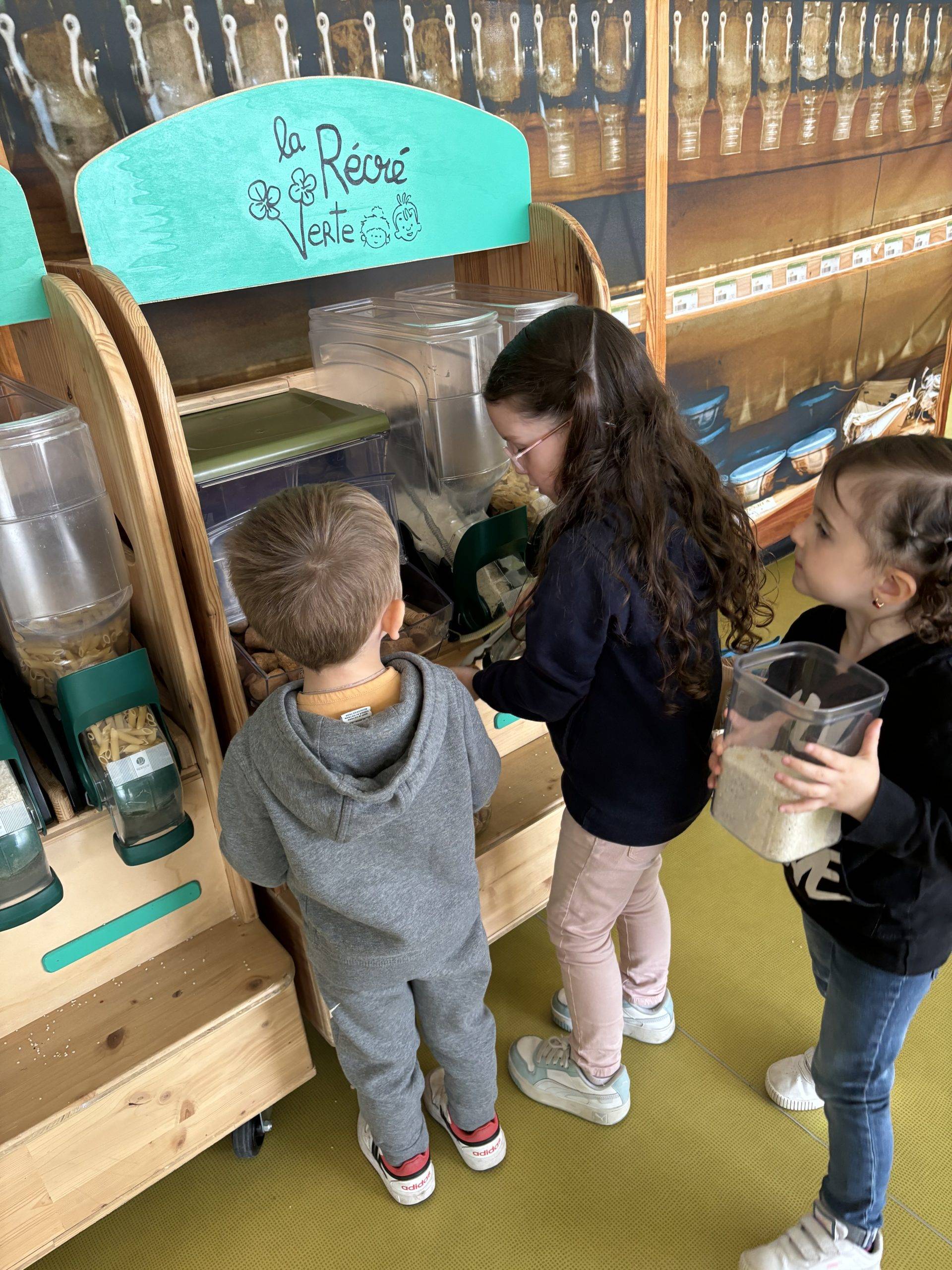 Les enfants apprennent à utiliser les distributeurs à vrac en se servant du riz et des pâtes.